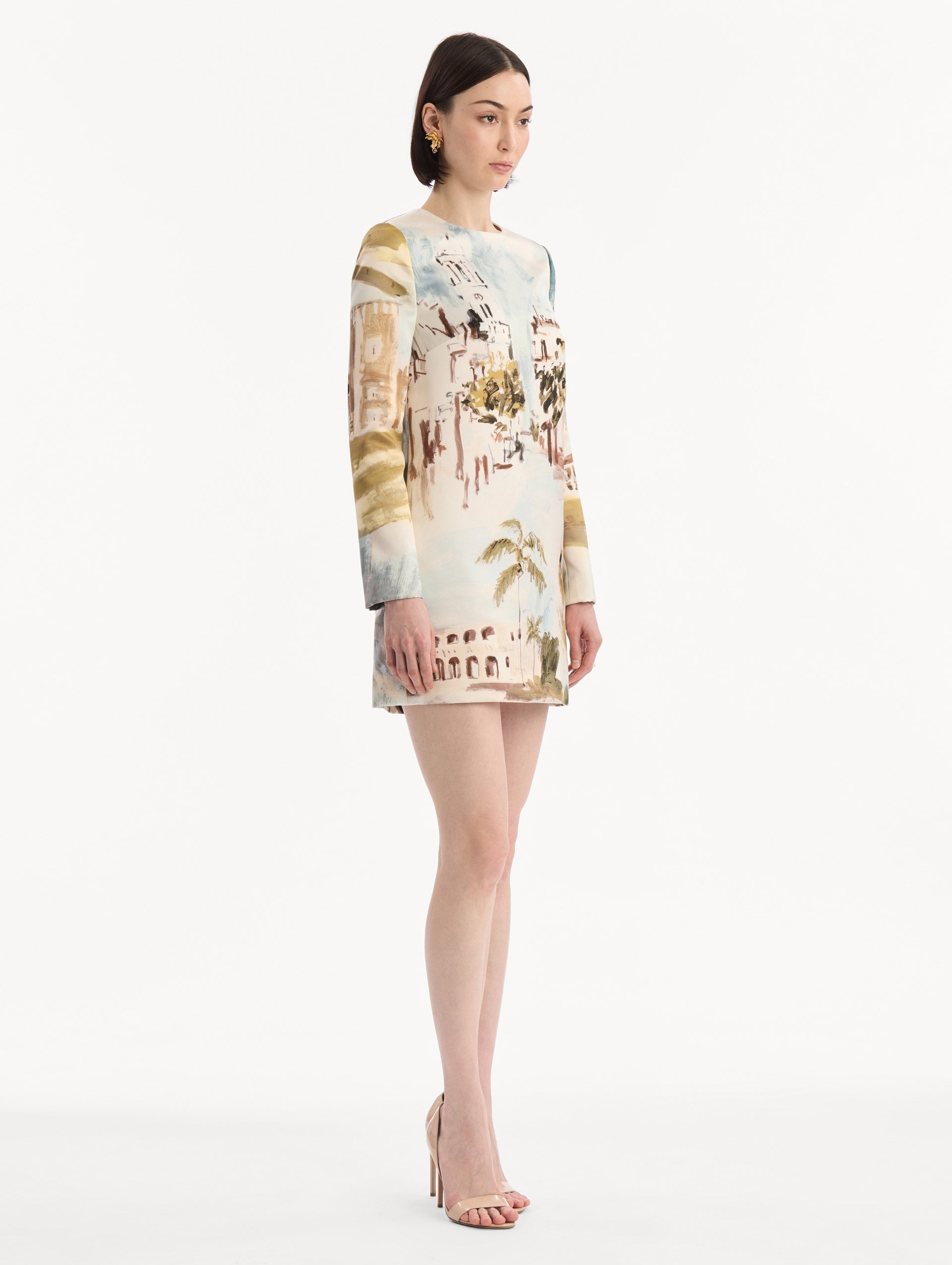 The model is wearing the Dominican Landscape Shift Dress. Featuring long sleeves and a mini length. Side View.