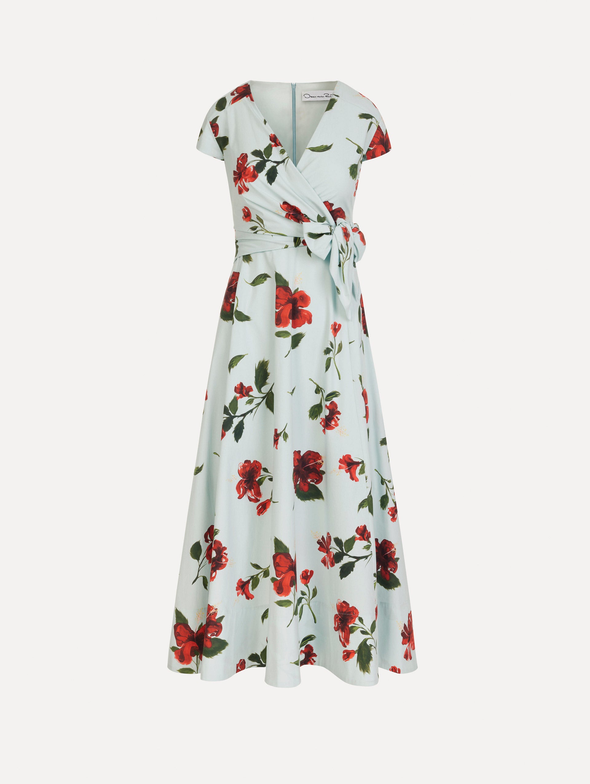 The Hibiscus Cotton Poplin Wrap Dress in light blue printed with red hibiscus blooms. Featuring a wrap construction bodice, cap sleeves, V-neckline, and full midi skirt. Front View.