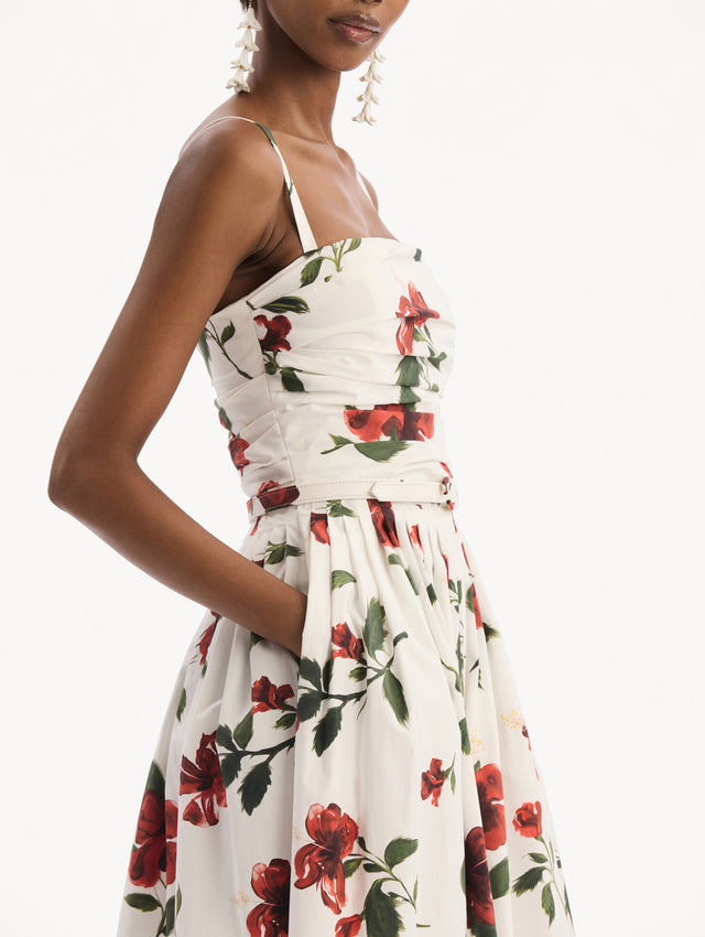 The model is wearing the Hibiscus Cotton Poplin Dress in white with red hibiscus blooms. Featuring a ruched bodice, tank straps, belt at waist, and full, gathered skirt. Detail View.