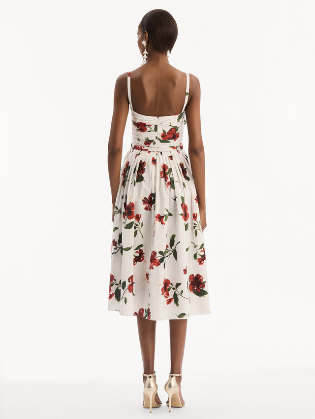 The model is wearing the Hibiscus Cotton Poplin Dress in white with red hibiscus blooms. Featuring a ruched bodice, tank straps, belt at waist, and full, gathered skirt. Back View.