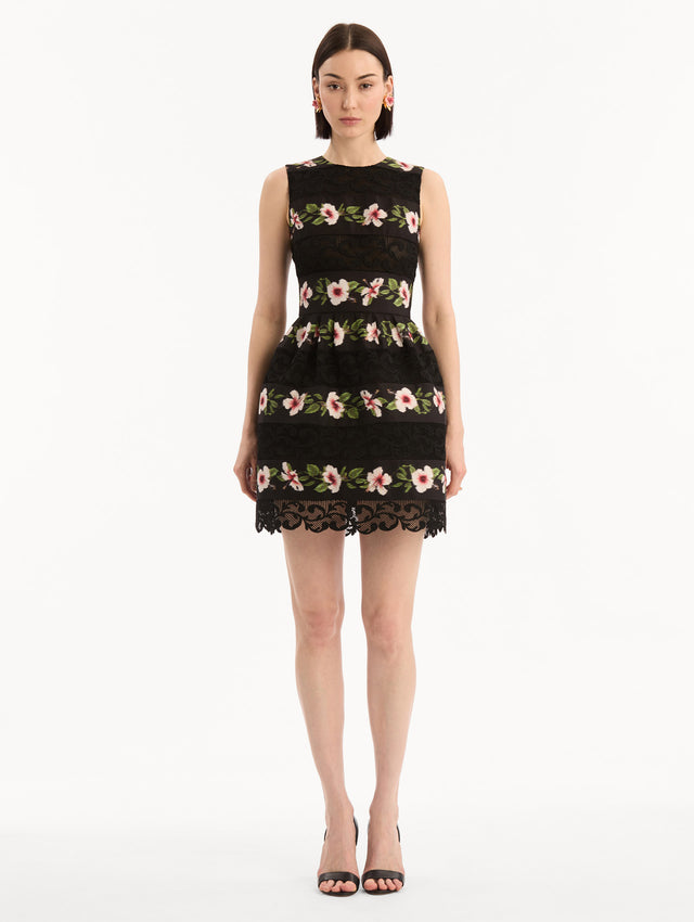 The model is wearing the Chiné Hibiscus Striped Faille Dress in Black. Featuring woven hibiscus motifs alternating with panels of faille and guipure lace, creating a striped pattern. Mini length. Front View.