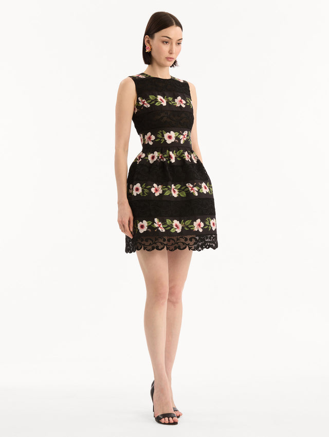 The model is wearing the Chiné Hibiscus Striped Faille Dress in Black. Featuring woven hibiscus motifs alternating with panels of faille and guipure lace, creating a striped pattern. Mini length. Side View.