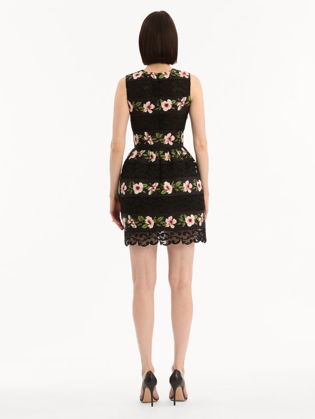 The model is wearing the Chiné Hibiscus Striped Faille Dress in Black. Featuring woven hibiscus motifs alternating with panels of faille and guipure lace, creating a striped pattern. Mini length. Back View.