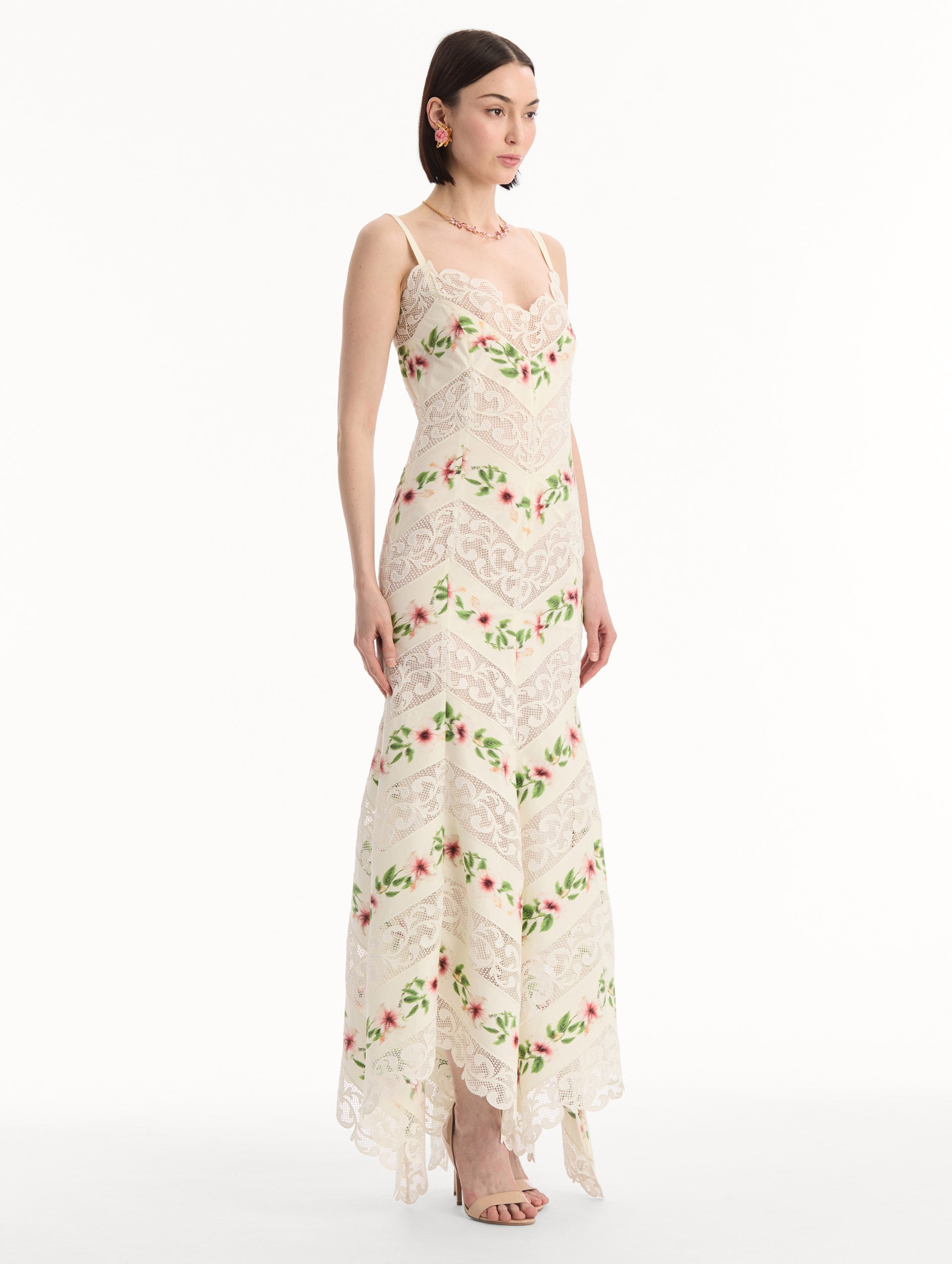 The model is wearing the Chiné Hibiscus Striped Cotton Poplin Dress in Ivory. Featuring a lace neckline, tank straps, and woven hibiscus motifs alternating with panels of faille and guipure lace, creating a striped composition. Side View.