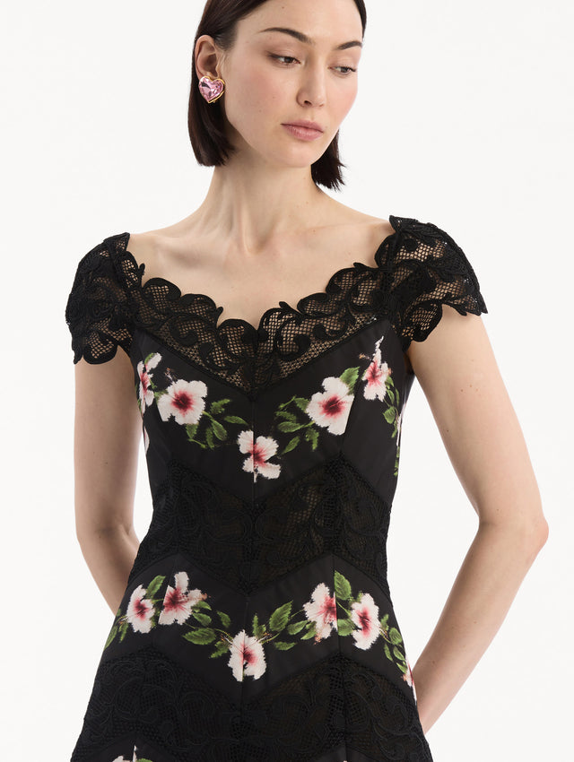 The model is wearing the Chiné Hibiscus Striped Faille Midi Dress in Black. Featuring off-the-shoulder cap sleeves, a midi length, and woven hibiscus motifs alternating with panels of faille and guipure lace, creating a striped composition. Detail View.