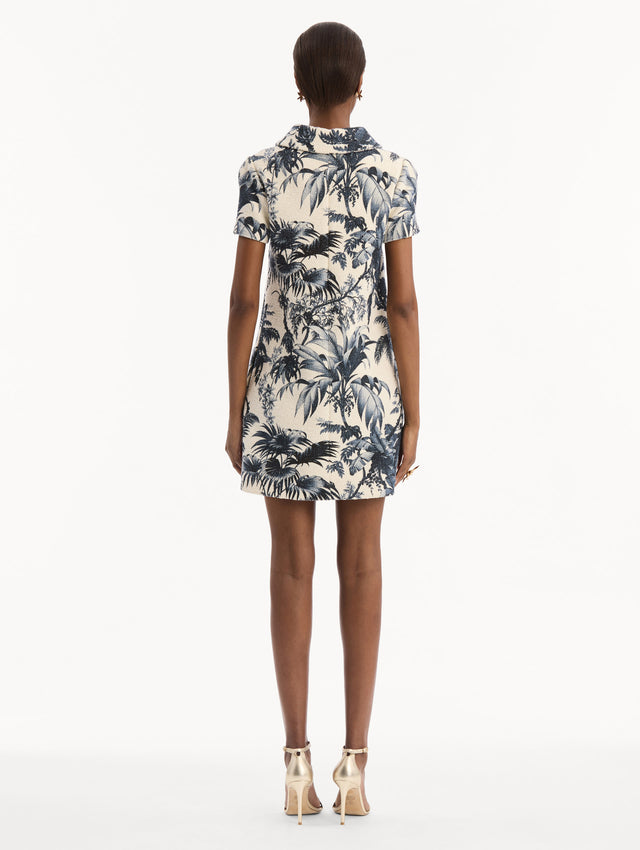 The model is wearing the Chiné Palm Leaves Shift Dress in ivory printed with navy palm leaves. Featuring a classic collar neckline, short sleeves, and mini length. Back View.
