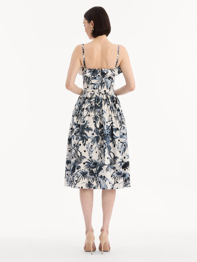 The model is wearing the Dotted Palm Leaves Cotton Poplin Sleeveless Dress in Navy Blue and White. Featuring a palm leaves print, ruffled top, delicate straps, belt at waist, softly structured bodice, and gathered skirt. Back View.