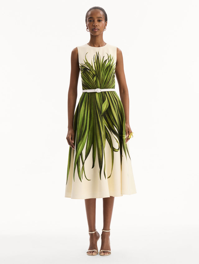 The model is wearing the Palm Leaves Wool-Blend Dress in ivory printed with green palm leaves. Featuring a belt at waist and midi-length skirt. Front View.