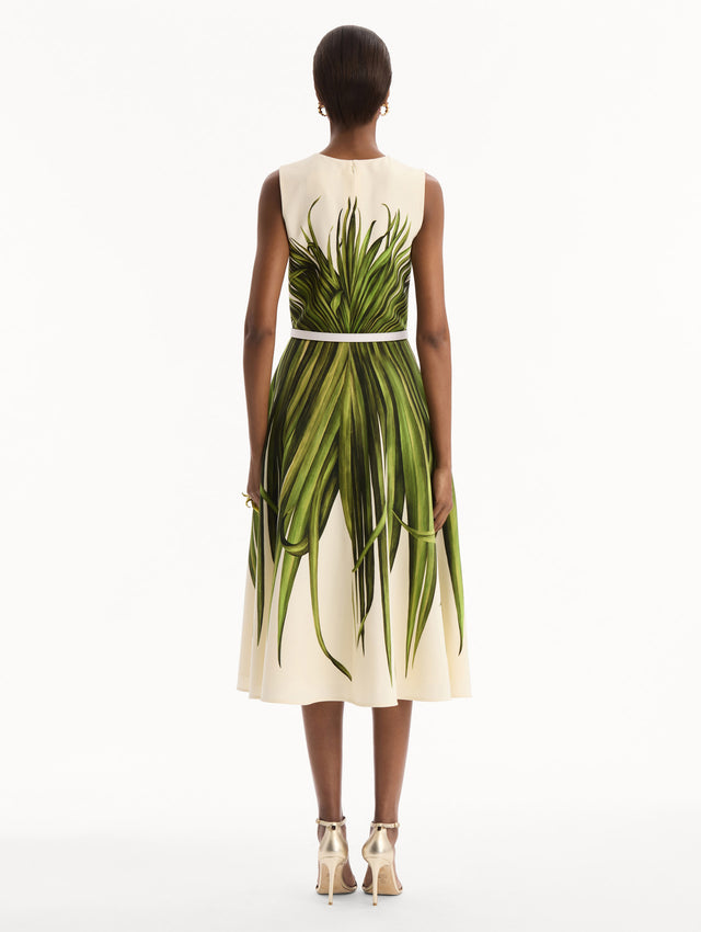 The model is wearing the Palm Leaves Wool-Blend Dress in ivory printed with green palm leaves. Featuring a belt at waist and midi-length skirt. Back View.