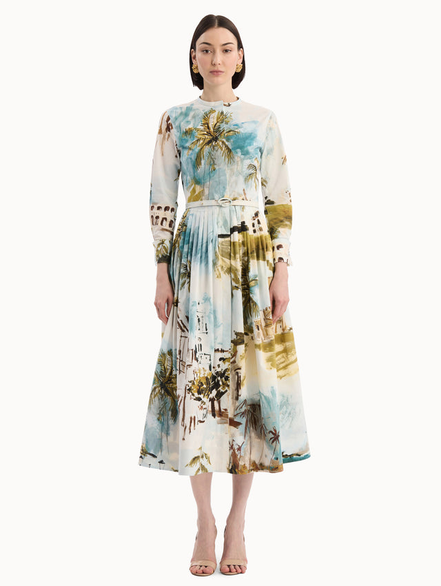 The model is wearing the Dominican Landscape Cotton Poplin Short-Sleeve Dress printed with the Dominican landscape. Featuring long sleeves, front-button closure, belt at waist, and pleated midi skirt. Front view.