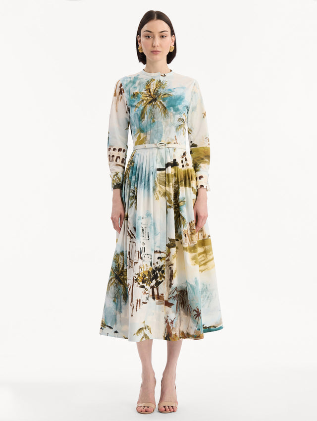 The model is wearing the Dominican Landscape Cotton Poplin Short-Sleeve Dress printed with the Dominican landscape. Featuring long sleeves, front-button closure, belt at waist, and pleated midi skirt. Front View.