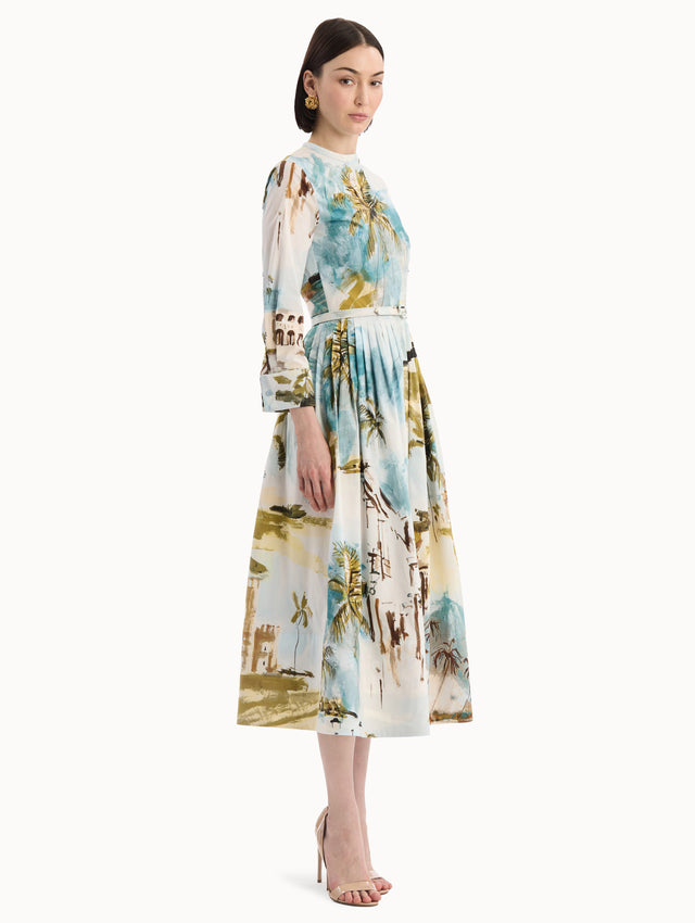 The model is wearing the Dominican Landscape Cotton Poplin Short-Sleeve Dress printed with the Dominican landscape. Featuring long sleeves, front-button closure, belt at waist, and pleated midi skirt. Side View.