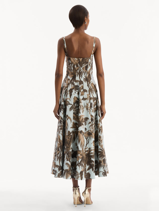 The model is wearing the Chiné Palm Leaves Cotton Poplin Dress in light blue printed with brown palm leaves. Featuring a subtle sweetheart neckline with tank straps, a softly structured bodice, and flowing midi skirt. Back View.