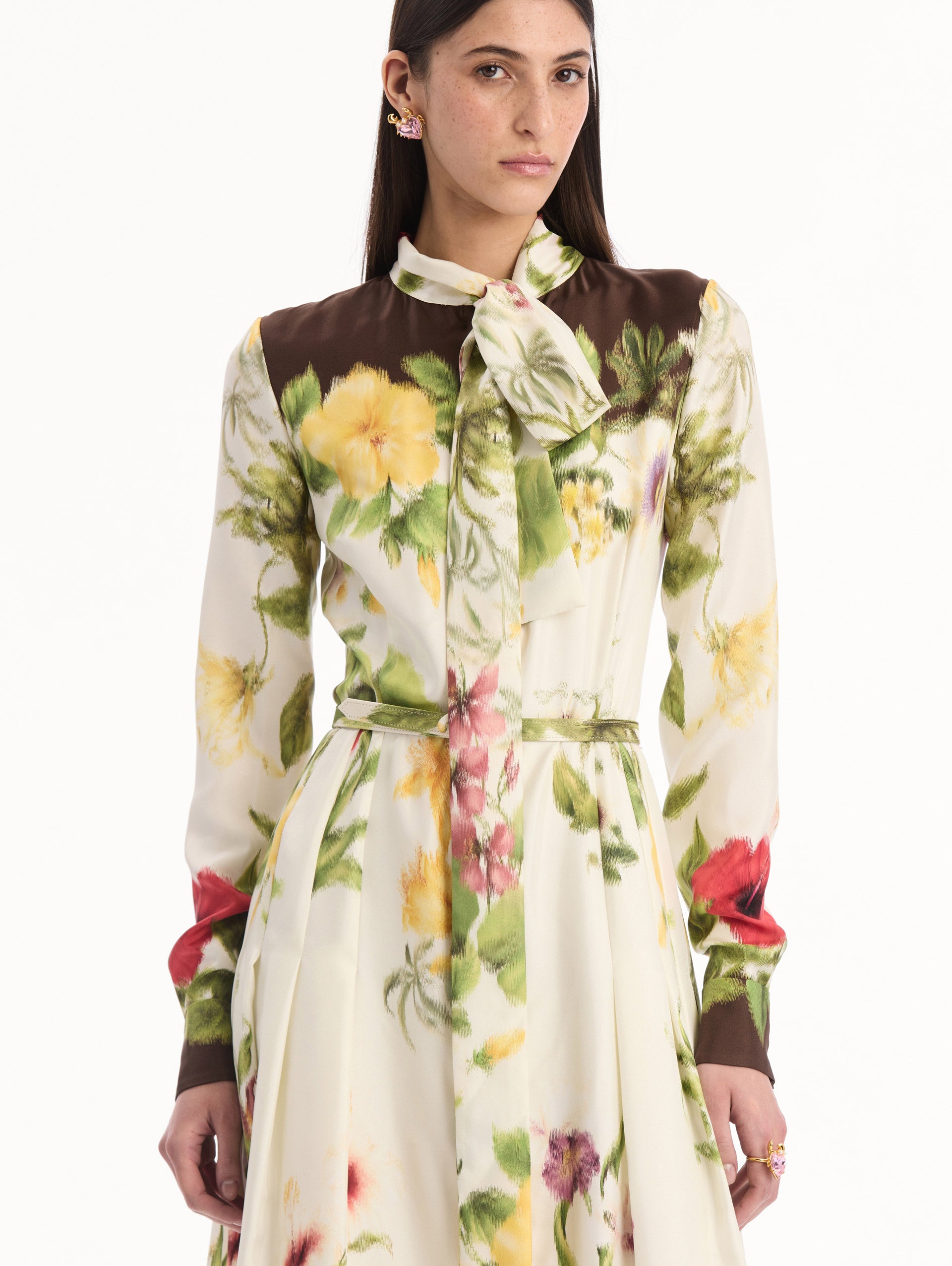 The model is wearing the Chiné Dominican Mixed-Floral Silk Twill Dress. Featuring a vibrant array of Dominican florals, tie neckline, belt at waist, long sleeves, and a midi length. Detail View.
