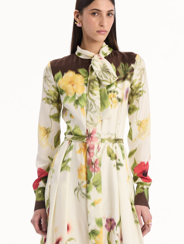The model is wearing the Chiné Dominican Mixed-Floral Silk Twill Dress. Featuring a vibrant array of Dominican florals, tie neckline, belt at waist, long sleeves, and a midi length. Detail View.