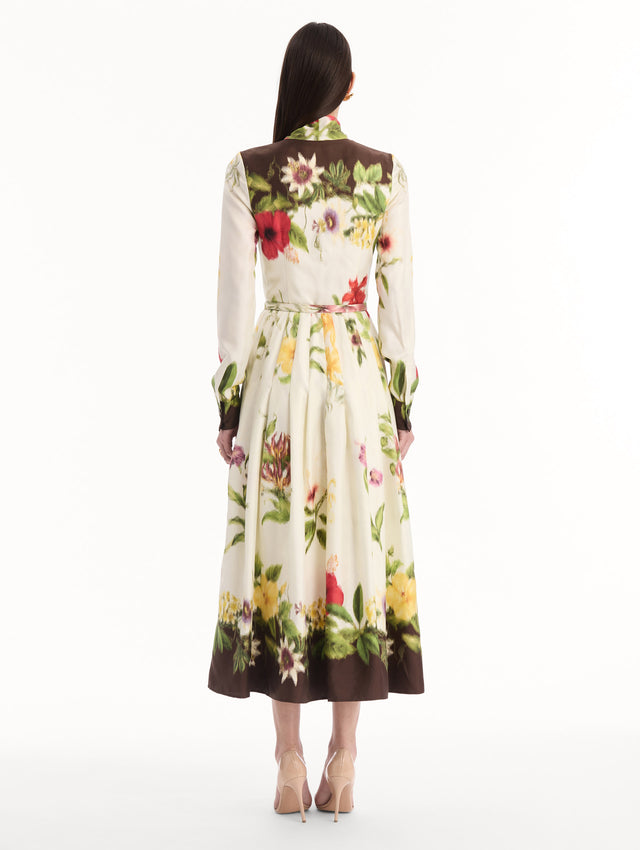 The model is wearing the Chiné Dominican Mixed-Floral Silk Twill Dress. Featuring a vibrant array of Dominican florals, tie neckline, belt at waist, long sleeves, and a midi length. Back View.