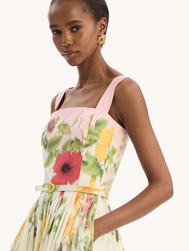 The model is wearing the Dominican Mixed-Floral Cotton Poplin Dress in ivory printed with an array of Dominican florals and light pink at the trims. Featuring a square neckline with tank straps, belt at waist, and pleated midi skirt. Detail View.