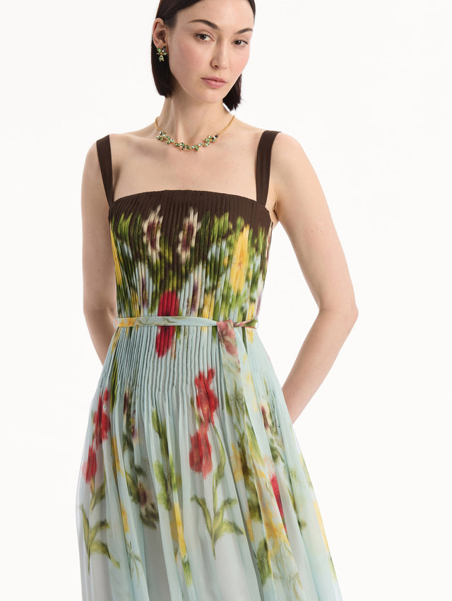 The model is wearing the Dominican Mixed-Floral Silk Chiffon Gown in light blue printed with an array of Dominican florals and brown at the trims. Featuring a pleated bodice, tank straps, tie at waist, and long, flowing skirt. Detail View.