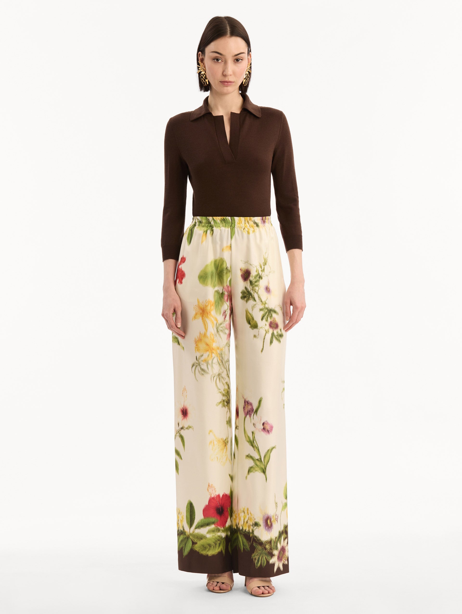 The model is wearing the Dominican Mixed-Floral Wide Leg Pant in ivory printed with an array of Dominican florals. Featuring wide legs and an elastic waistband. Front View.