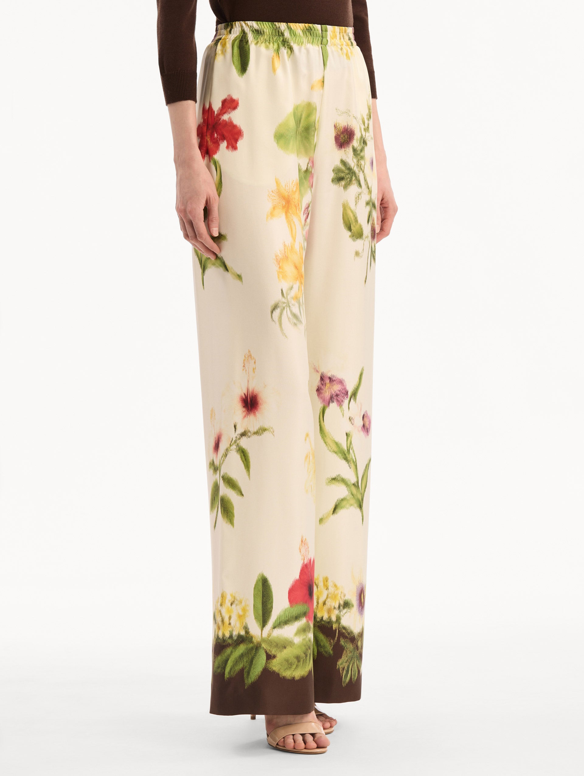The model is wearing the Dominican Mixed-Floral Wide Leg Pant in ivory printed with an array of Dominican florals. Featuring wide legs and an elastic waistband. Side View.
