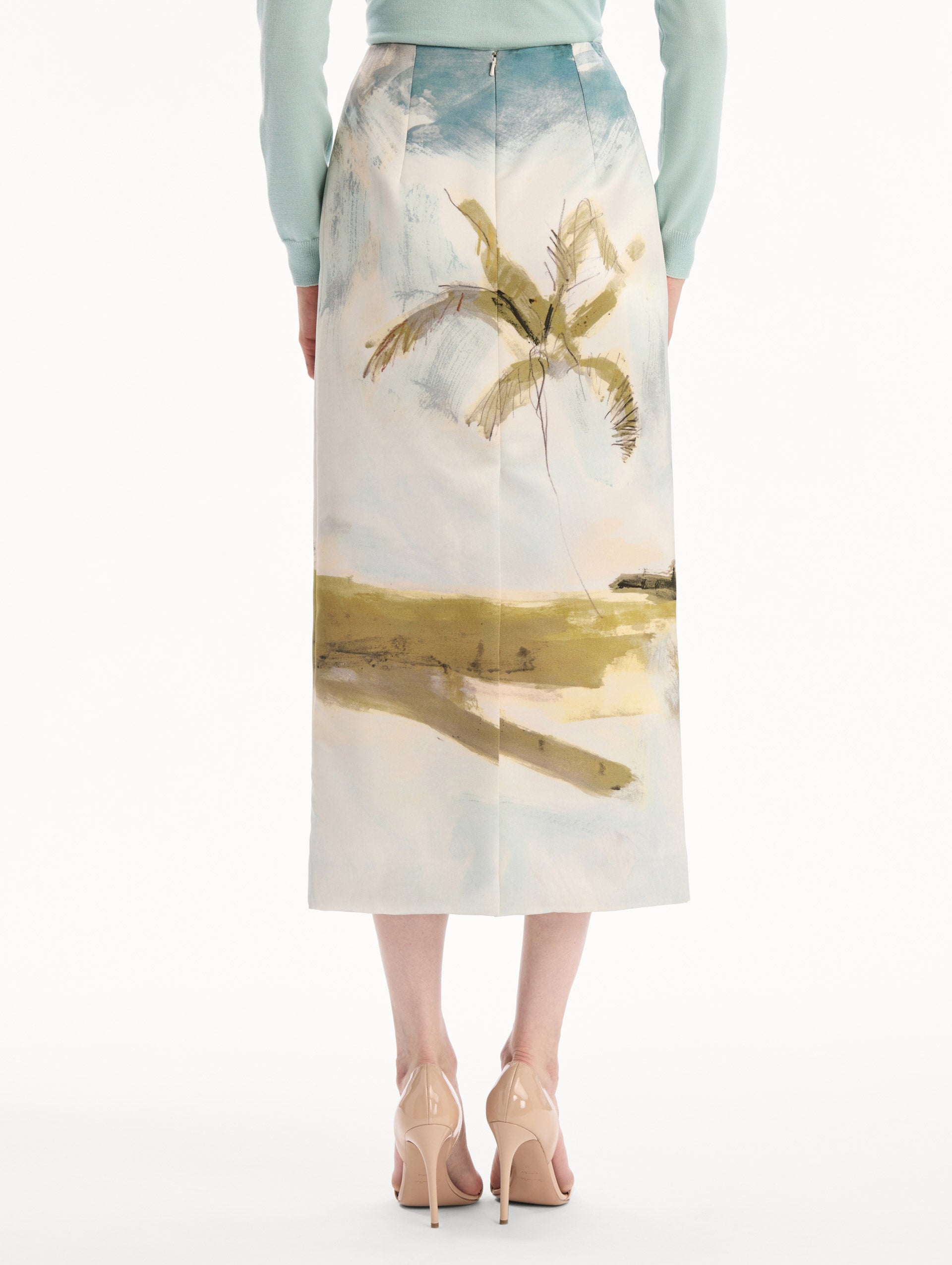 The model is wearing the Dominican Landscape Pencil Skirt printed in the Dominican landscape. Featuring a structured, column silhouette and midi length. Back View.