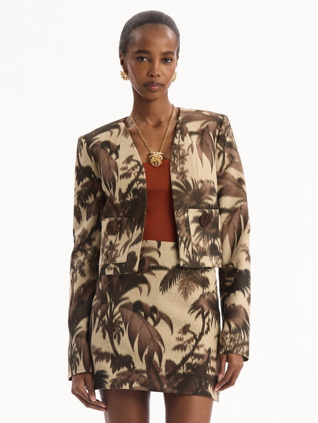 The model is wearing the Chiné Palm Leaves Jacket printed with brown palm leaves. Featuring long sleeves, front pockets with a button closure, and a tailored silhouette. Front View.