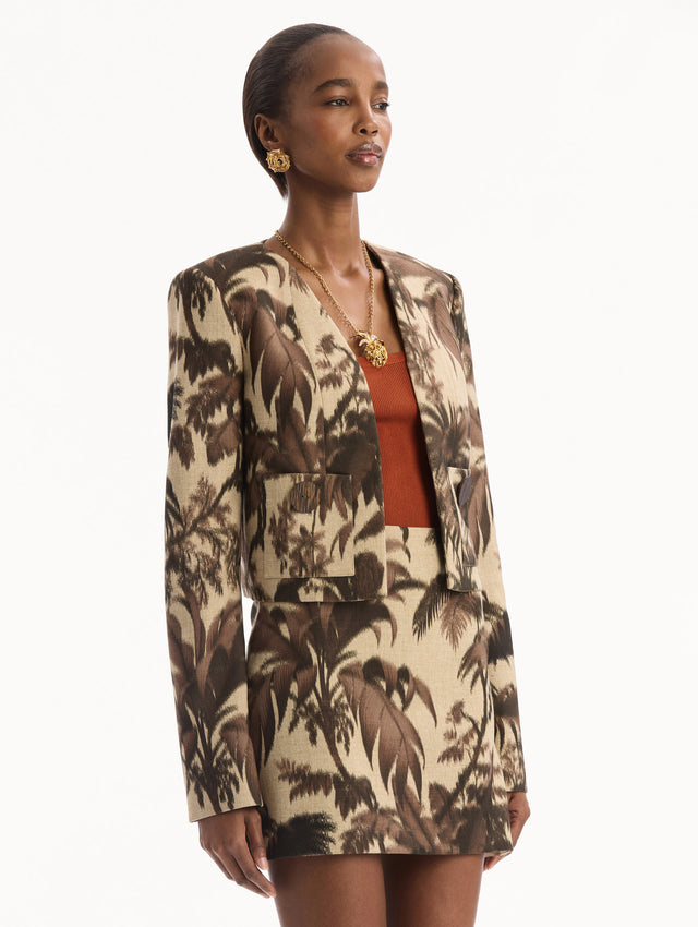 The model is wearing the Chiné Palm Leaves Jacket printed with brown palm leaves. Featuring long sleeves, front pockets with a button closure, and a tailored silhouette. Side View.