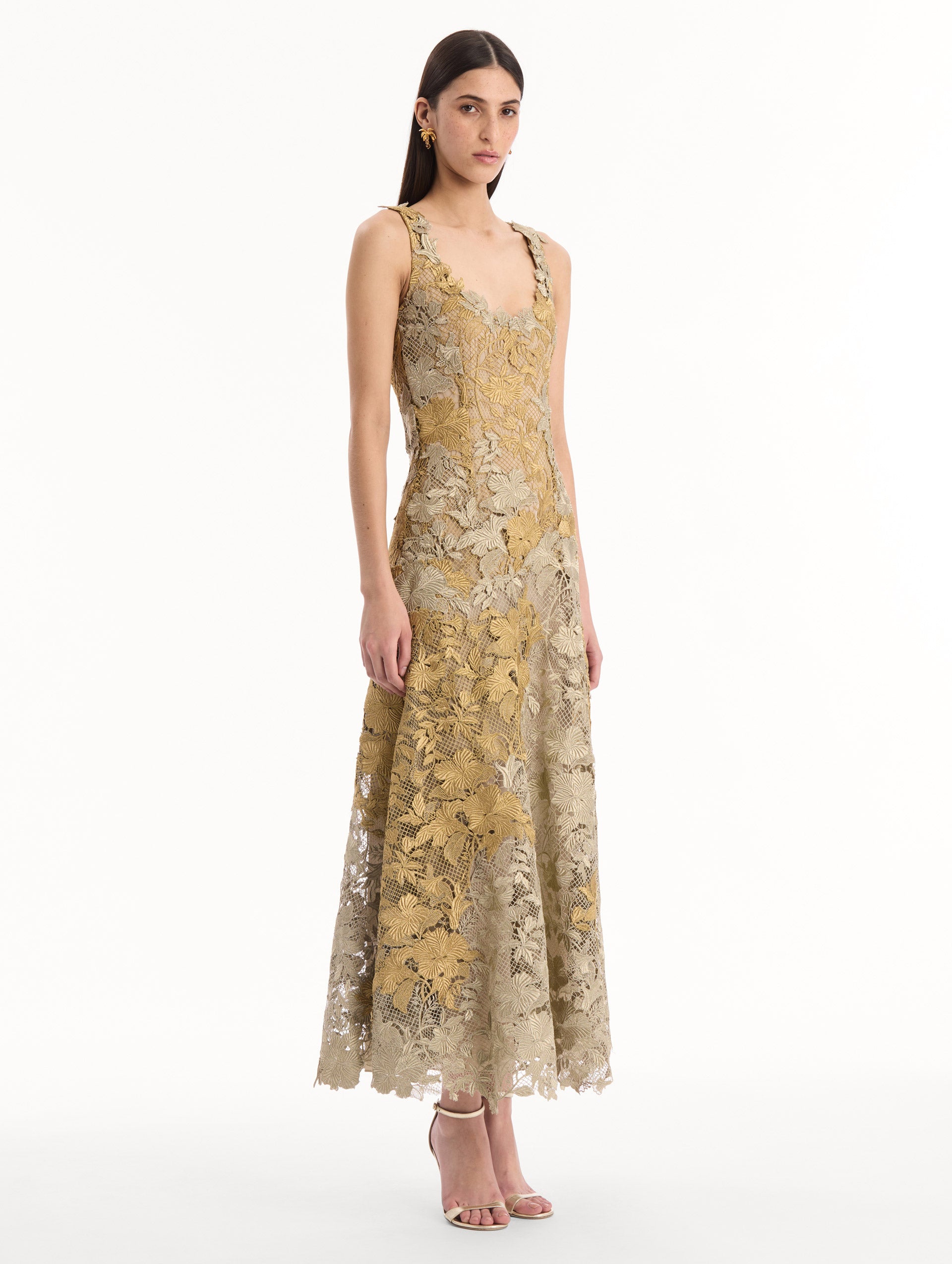 The model is wearing the Hibiscus Metallic Guipure Cocktail Dress in Gold. Featuring metallic guipure lace, a fitted bodice, and softly flared skirt. Side View.