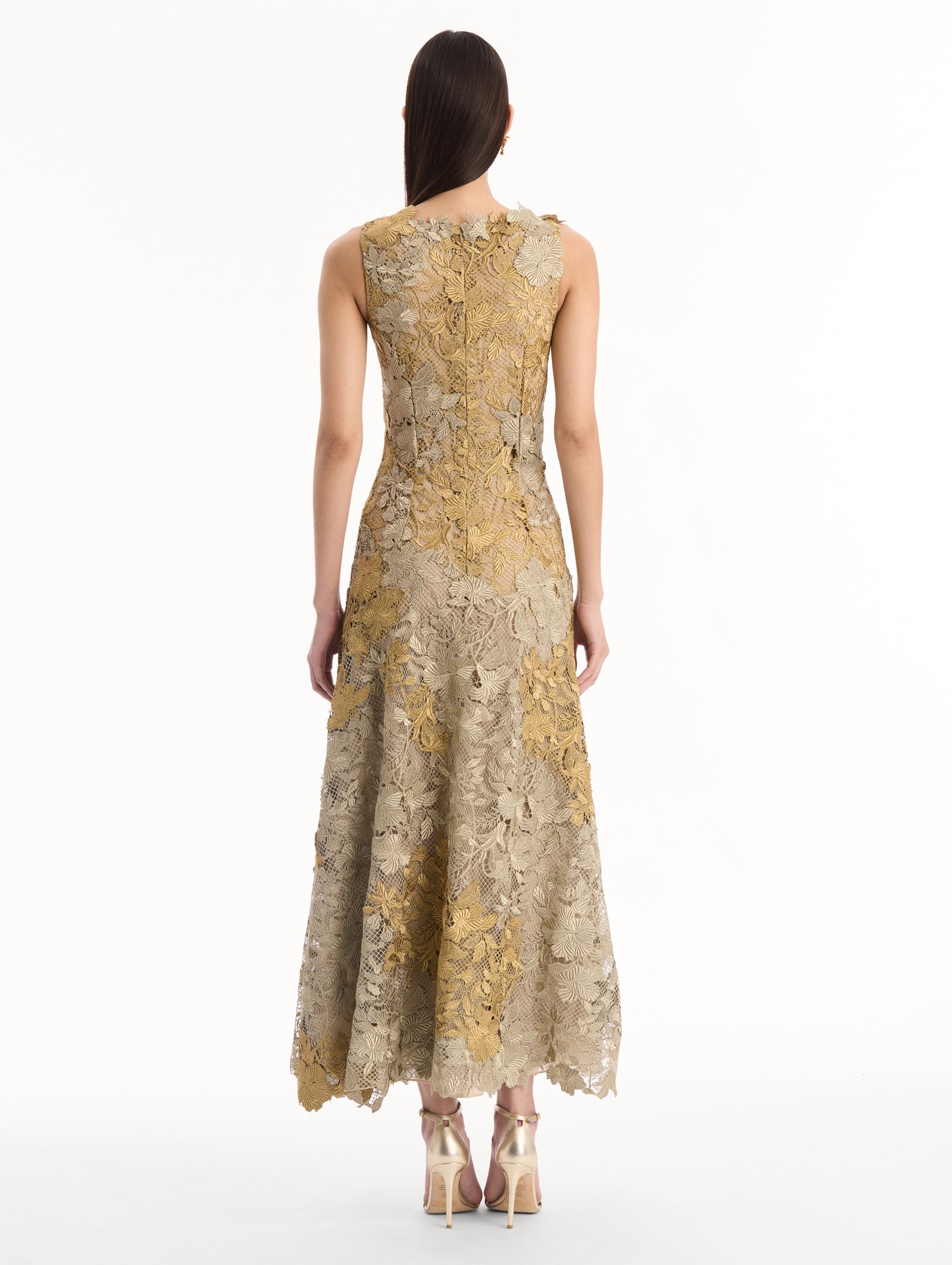 The model is wearing the Hibiscus Metallic Guipure Cocktail Dress in Gold. Featuring metallic guipure lace, a fitted bodice, and softly flared skirt. Back View.