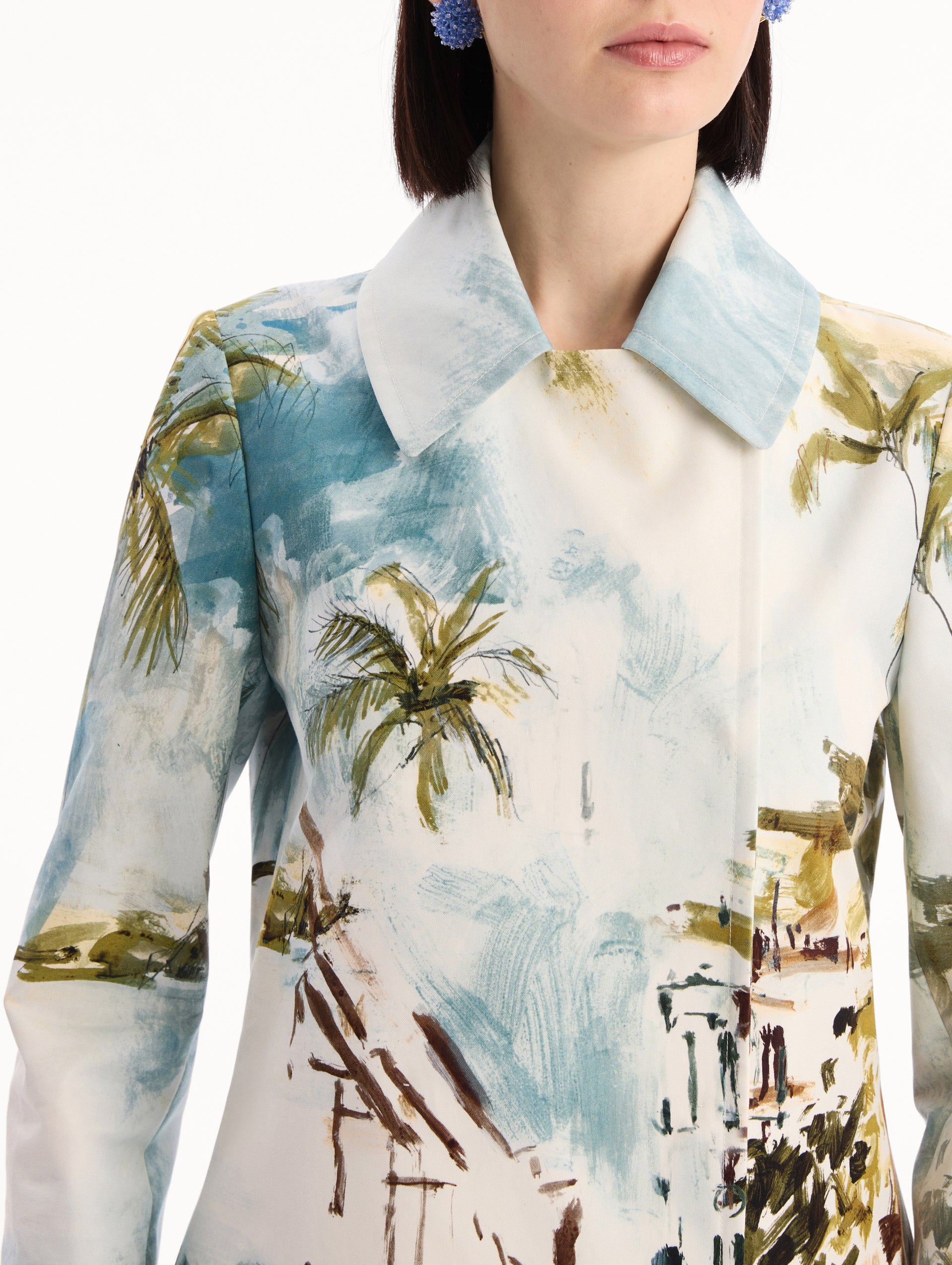 The model is wearing the Dominican Landscape Cotton Poplin Coat featuring an exaggerated collar, hidden buttons, front-flap pockets, and long sleeves. Detail View.