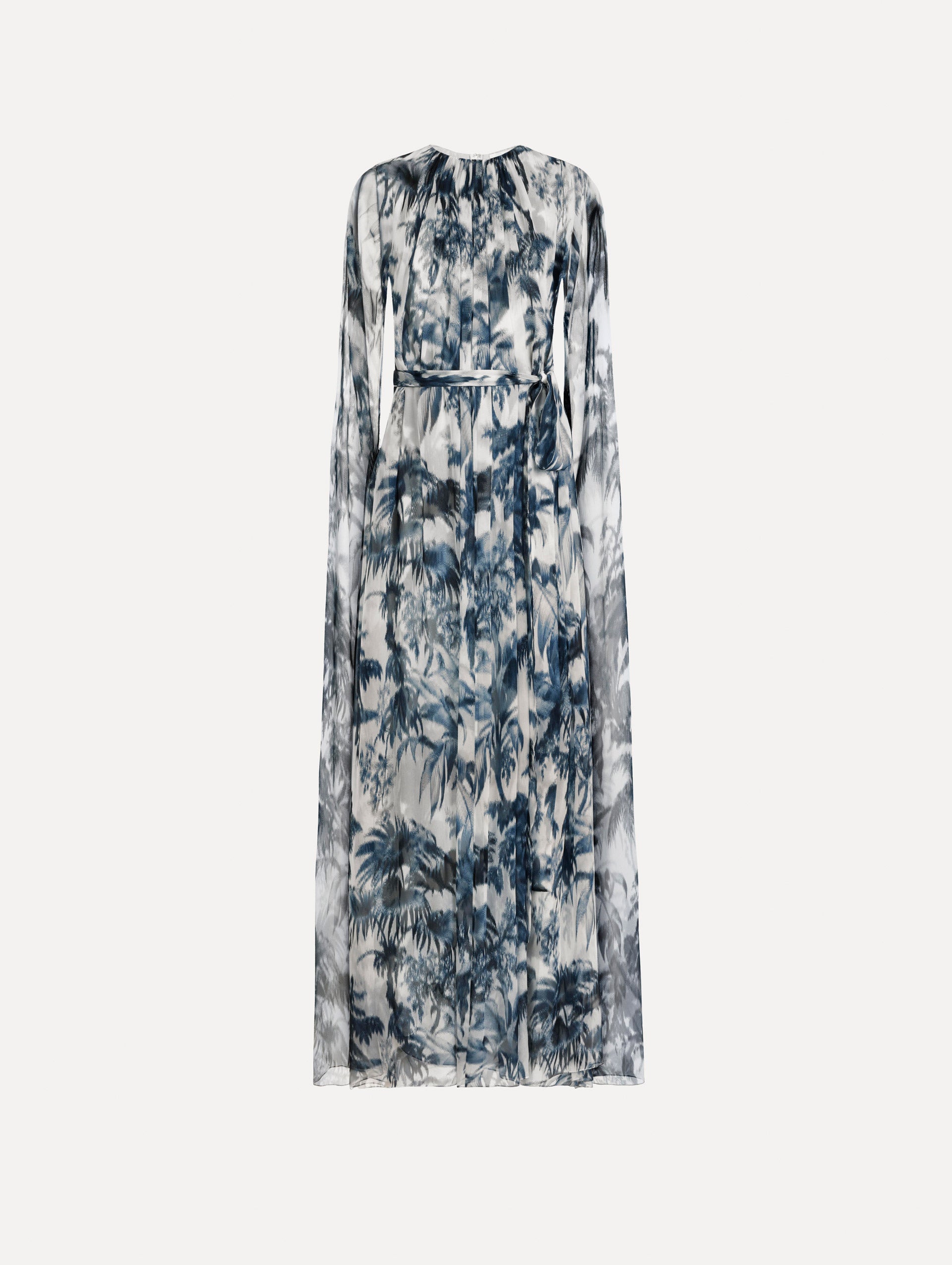 The Chiné Palm Leaves Silk Caftan White with Navy printed palm leaves. Featuring a gathered neckline, cape at back, flowing silhouette, and tie at waist. Front View.