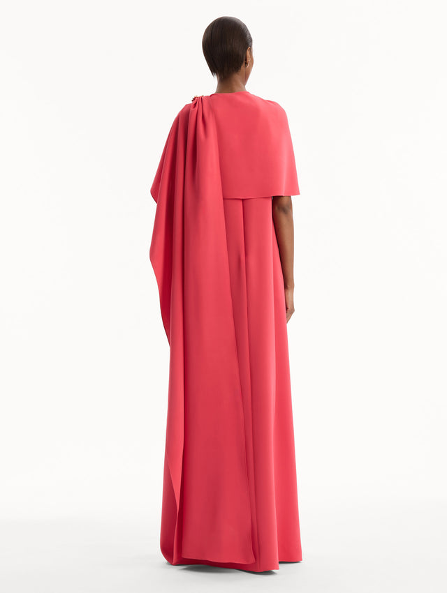 The model is wearing the Hibiscus Brooch Georgette Caftan in Hot Pink. Featuring a softly structured cape silhouette and a sculptural hibiscus brooch accent at the shoulder. Back View.