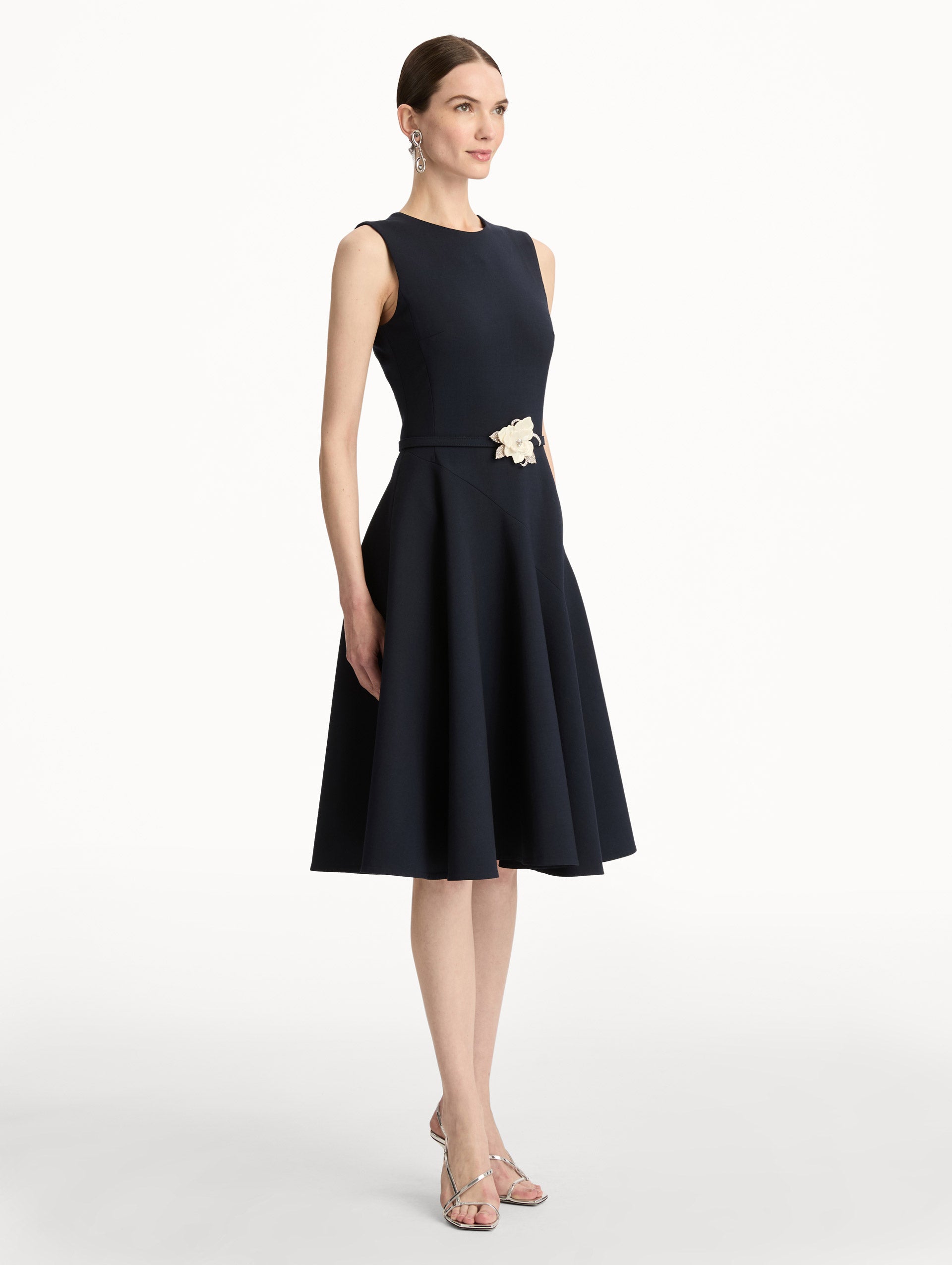 Black Floral Belt Sleeveless Dress featuring a belted waist with a white floral embellishment and a knee-length skirt. Side View.