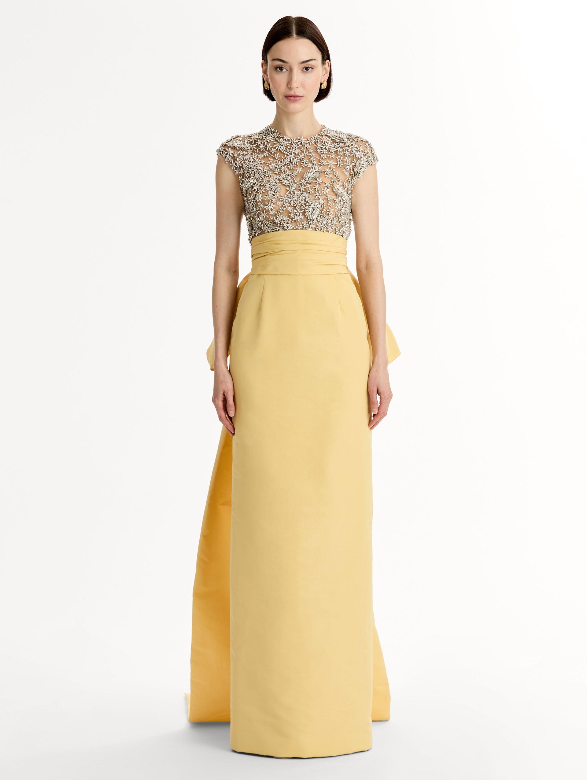 Yellow floor length gown with crystal porcelain flowers on an open back sculpted bodice. Dramatic faille skirt with cascading peplum train. Front View.