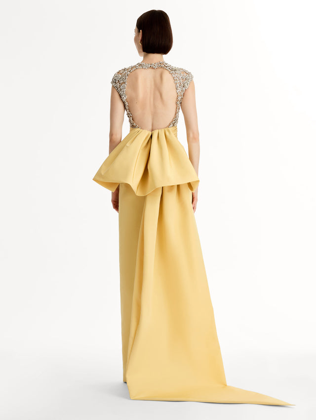 Yellow floor length gown with crystal porcelain flowers on an open back sculpted bodice. Dramatic faille skirt with cascading peplum train. Back View.