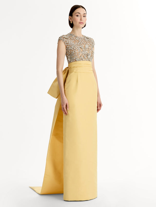Yellow floor length gown with crystal porcelain flowers on an open back sculpted bodice. Dramatic faille skirt with cascading peplum train. Side View.