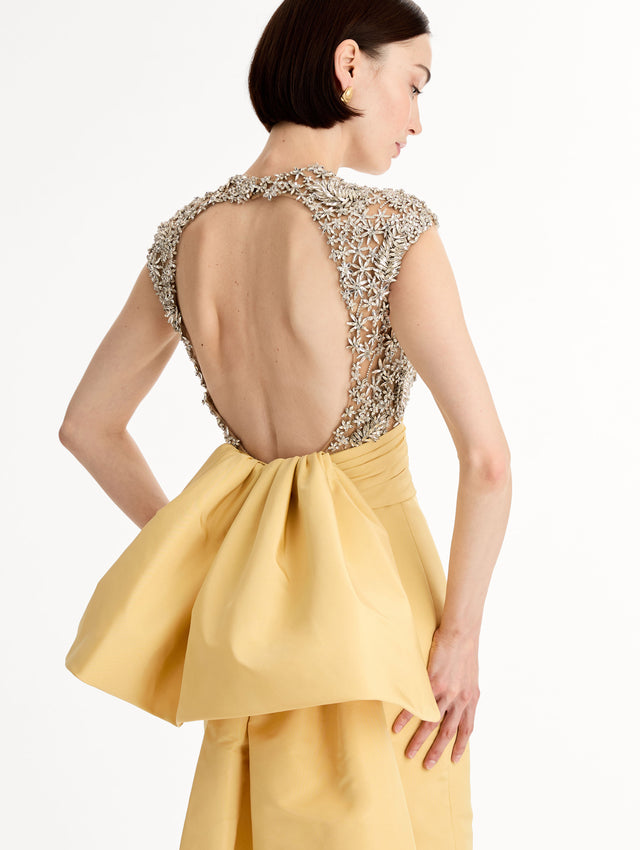 Yellow floor length gown with crystal porcelain flowers on an open back sculpted bodice. Dramatic faille skirt with cascading peplum train. Back View, Close Up.