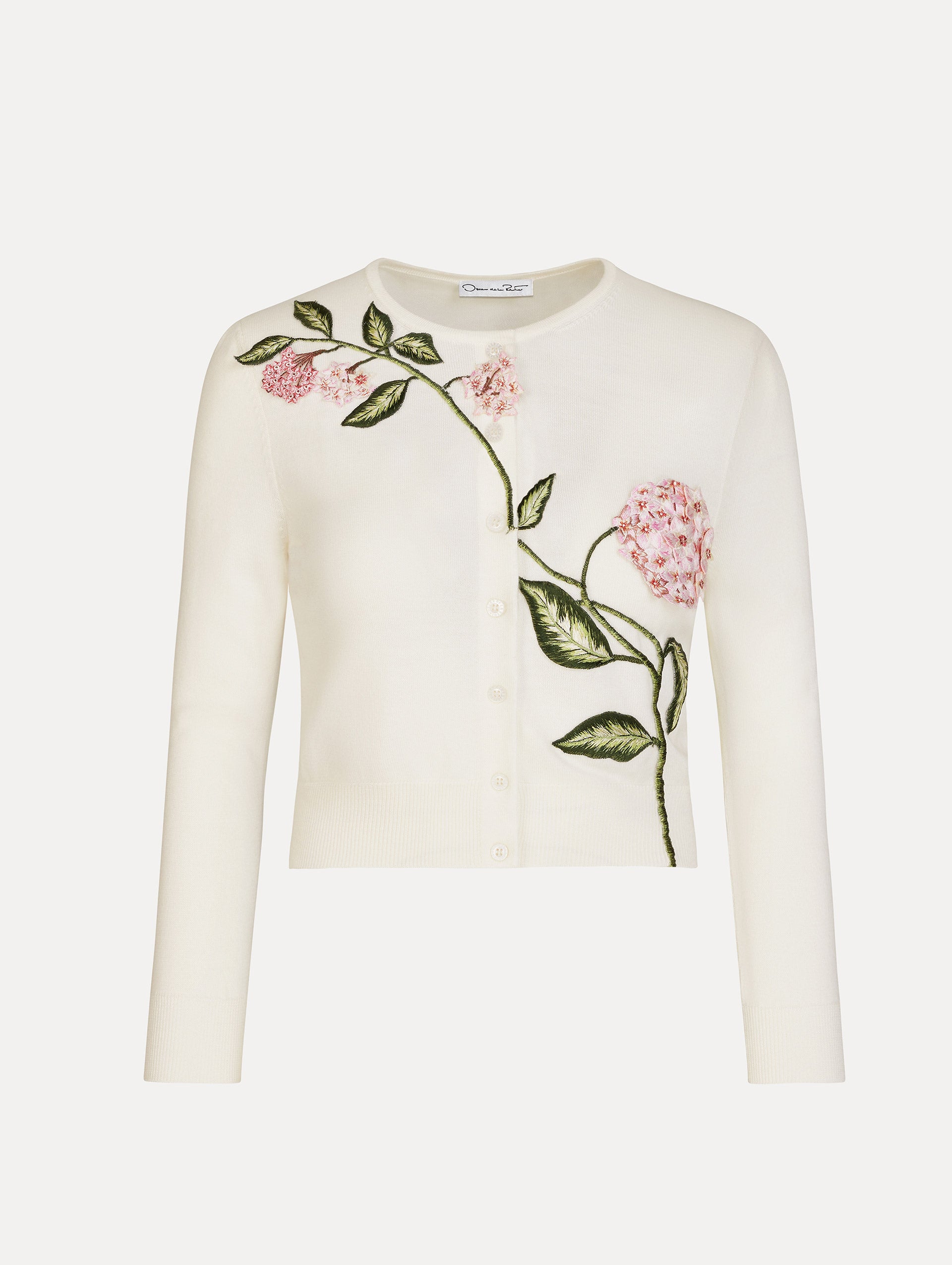Ivory cropped cardigan with pink flower detailing stitched along the neckline and shoulder. Classic button closure. Crew Neck. Front View. 