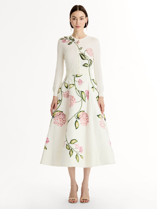 Ivory cropped cardigan with pink flower detailing stitched along the neckline and shoulder. Classic button closure. Crew Neck. Front View. 