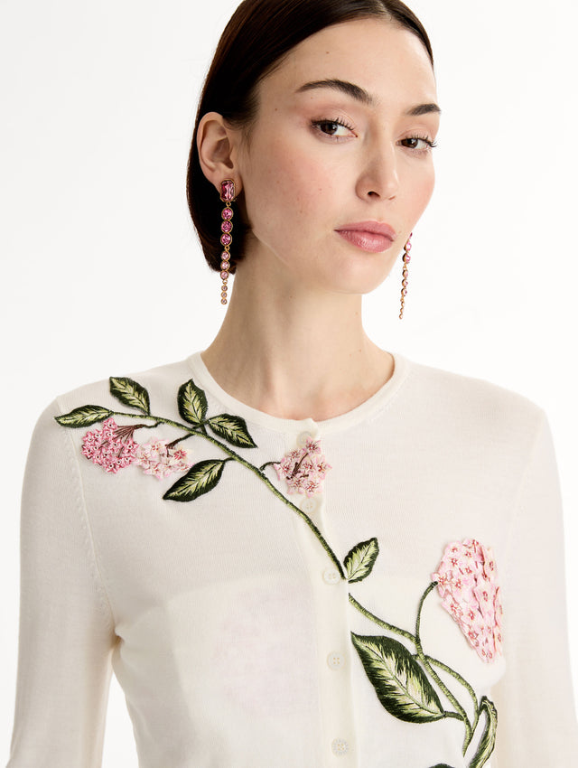 Ivory cropped cardigan with pink flower detailing stitched along the neckline and shoulder. Classic button closure. Crew Neck. Front View, Close Up. 