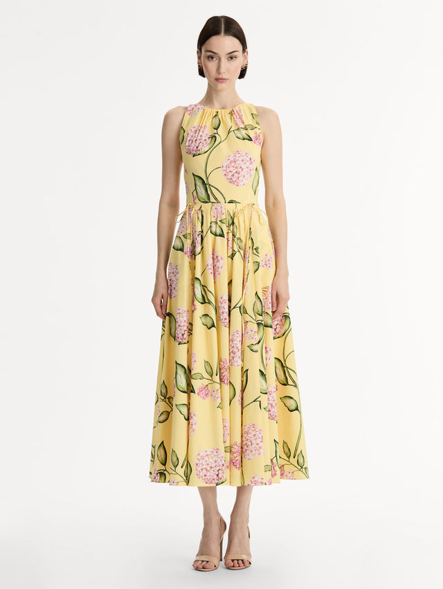 Halter neck, sleeveless, cotton poplin midi dress in yellow. Pleated with vivid pink flower print. Subtle bows at waist. Front View.
