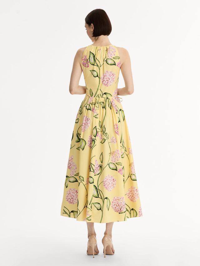 Halter neck, sleeveless, cotton poplin midi dress in yellow. Pleated with vivid pink flower print. Subtle bows at waist. Back View.