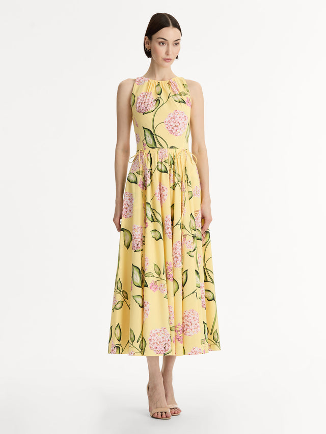 Halter neck, sleeveless, cotton poplin midi dress in yellow. Pleated with vivid pink flower print. Subtle bows at waist. Front View.