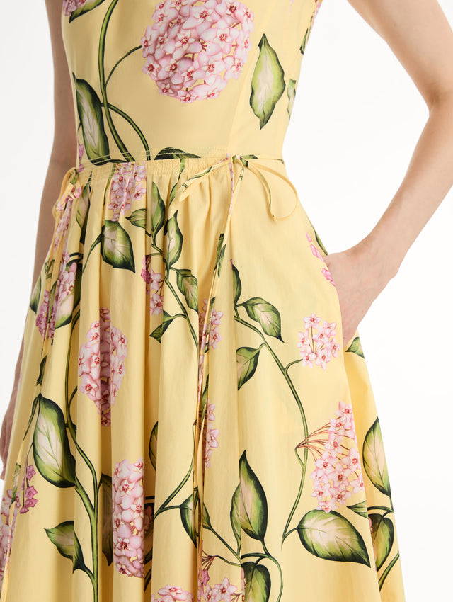 Halter neck, sleeveless, cotton poplin midi dress in yellow. Pleated with vivid pink flower print. Subtle bows at waist. Side View, Close Up.