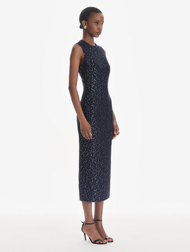 The model is wearing a sleeveless sequin tweed cocktail dress in navy. Side view.