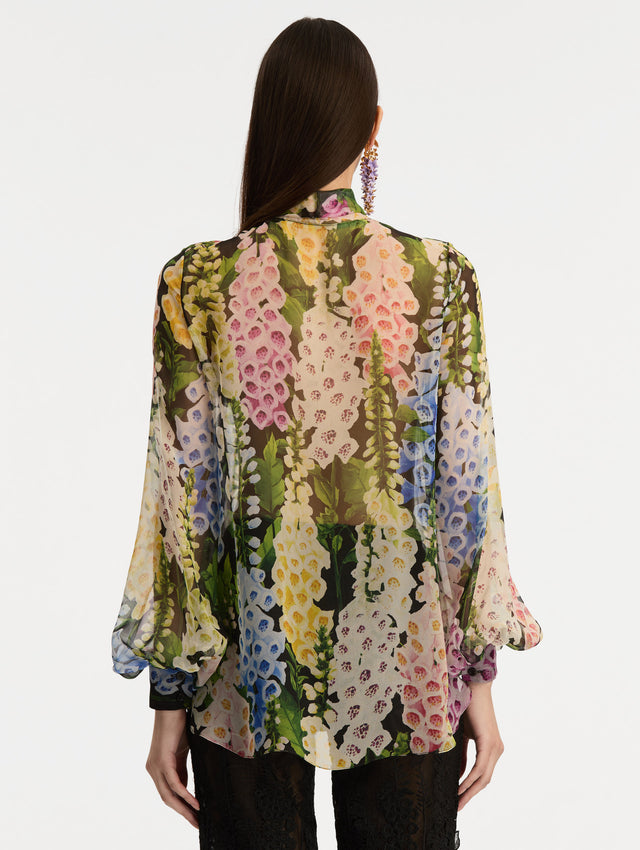 Black and floral Foxglove Tie-Neck Chiffon Blouse with billowing long sleeves with cuffed wrists. Back View.