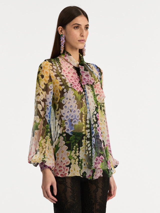 Black and floral Foxglove Tie-Neck Chiffon Blouse with billowing long sleeves with cuffed wrists. Side View.