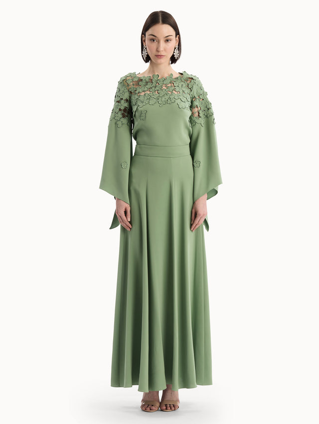 The model is wearing the Floral Appliqué Lattice Blouse in green featuring a floral, open lattice neckline and long, flowy sleeves. Front View.