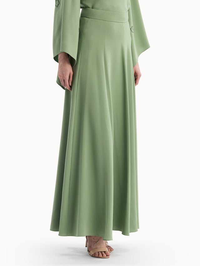 The model is wearing the Silk Georgette Midi Skirt in the color green featuring a high-waist and classic, flowing skirt. Side View.