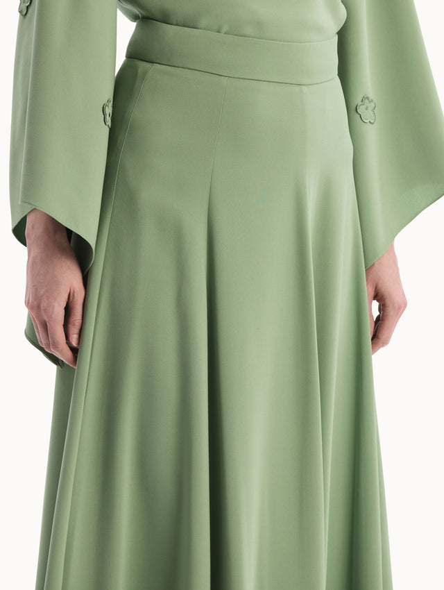 The model is wearing the Silk Georgette Midi Skirt in the color green featuring a high-waist and classic, flowing skirt. Side View.